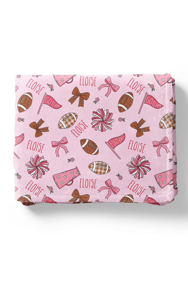 Caden Lane personalized baby blanket in pink football print, folded, featuring footballs, bows, pom poms, megaphones, and the custom name "Eloise.