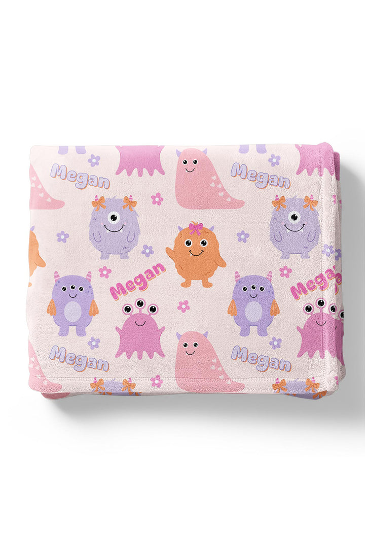 Folded Caden Lane personalized "Megan" minky blanket in Little Monsters print with pink, purple, and orange cartoon monsters and flowers
