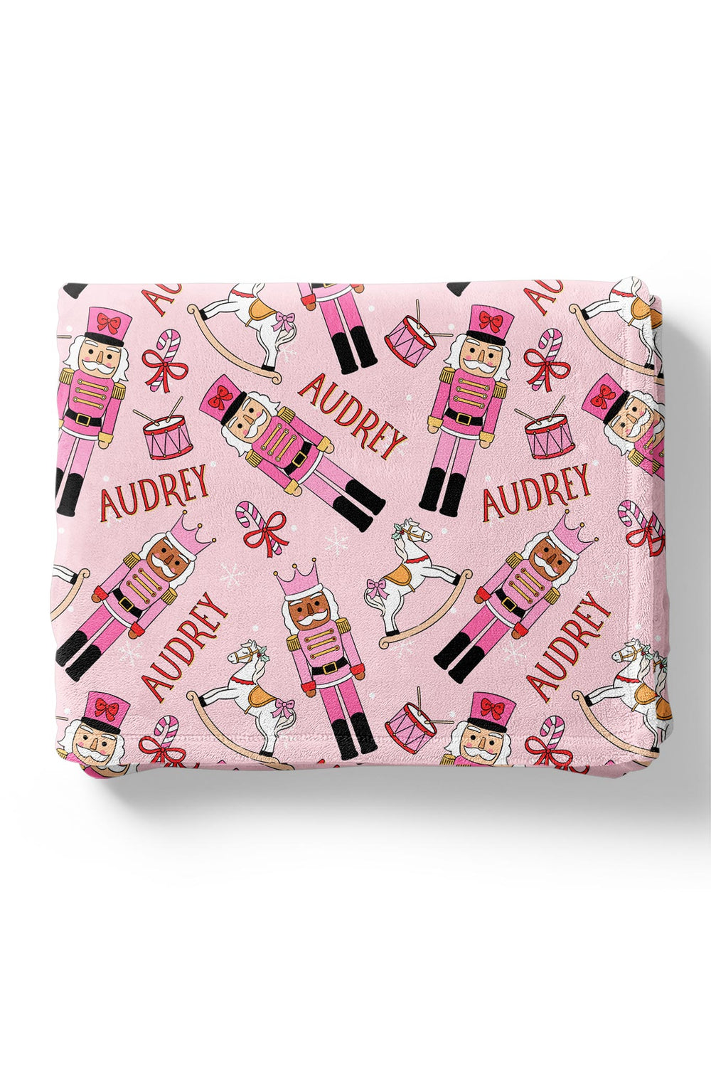 Personalized Caden Lane Christmas blanket featuring pink nutcrackers, rocking horses, drums, bows, snowflakes, and a custom child’s name.