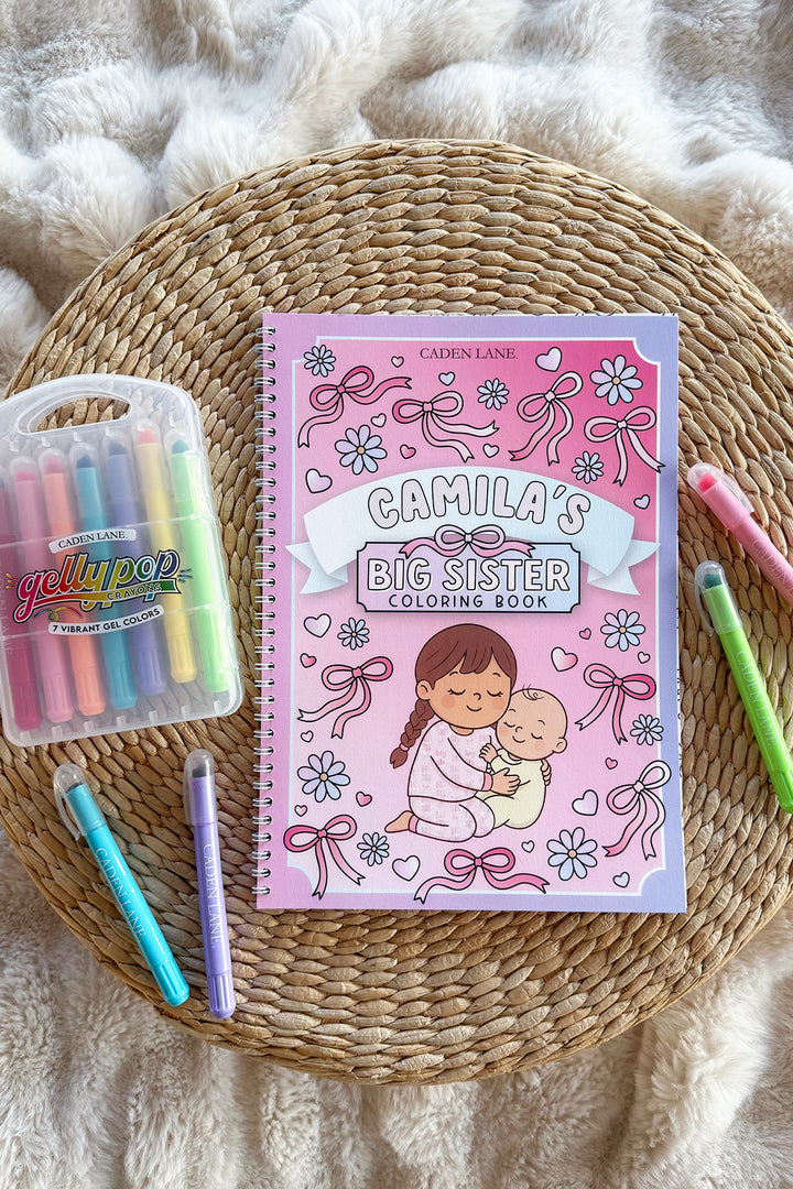 Caden Lane 'Camila's Big Sister Coloring Book' on a woven tray with a cream throw, Gellypop gel crayon case, and pastel Caden Lane markers