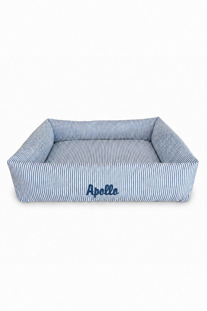 A square Lane & Leash pet bed with a blue and white striped fabric, featuring the name 'Apelle' embroidered in navy blue on the front, set against a plain white background.