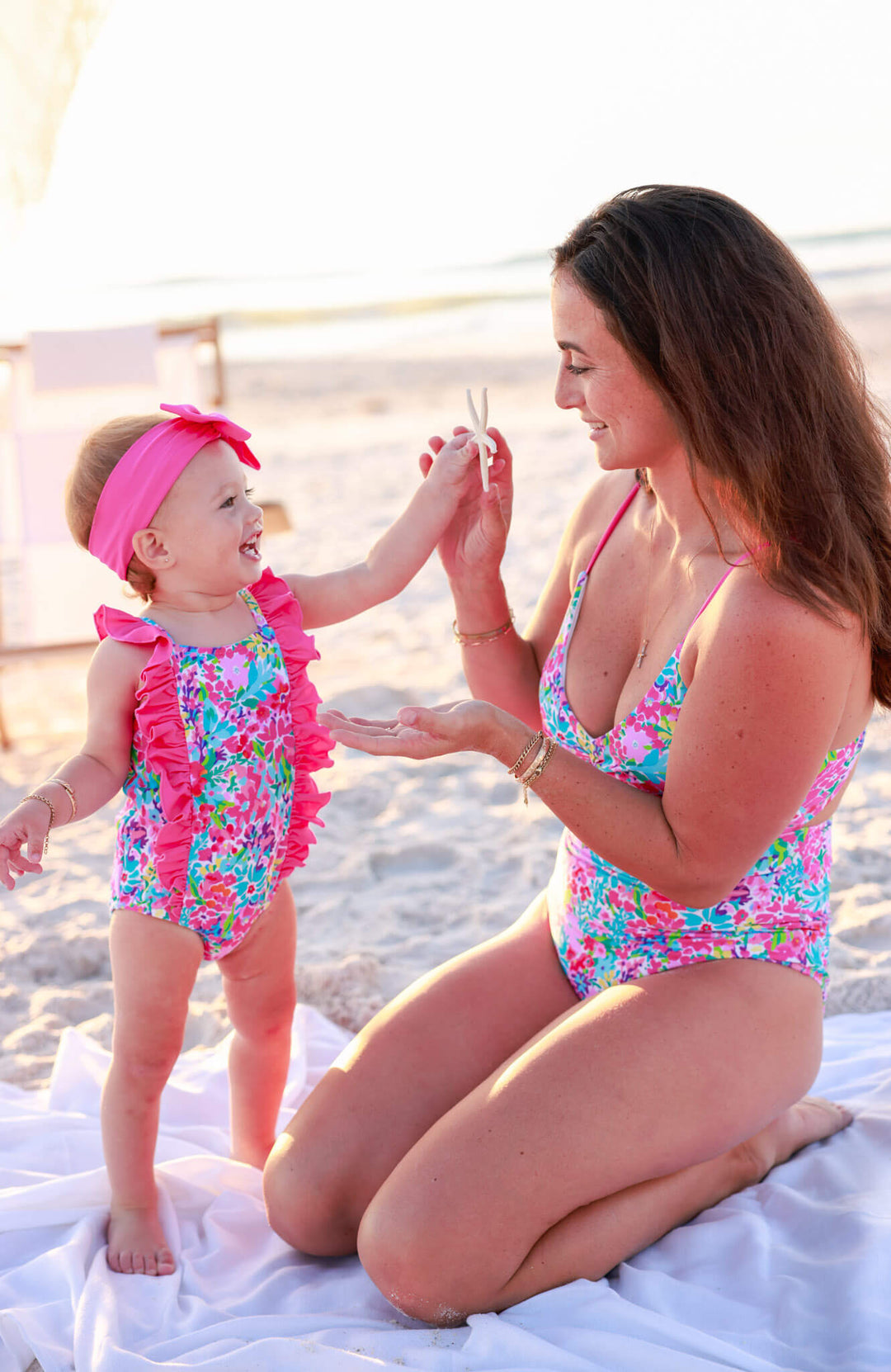 mom and daughter on the beach in matching bright floral swimsuits 