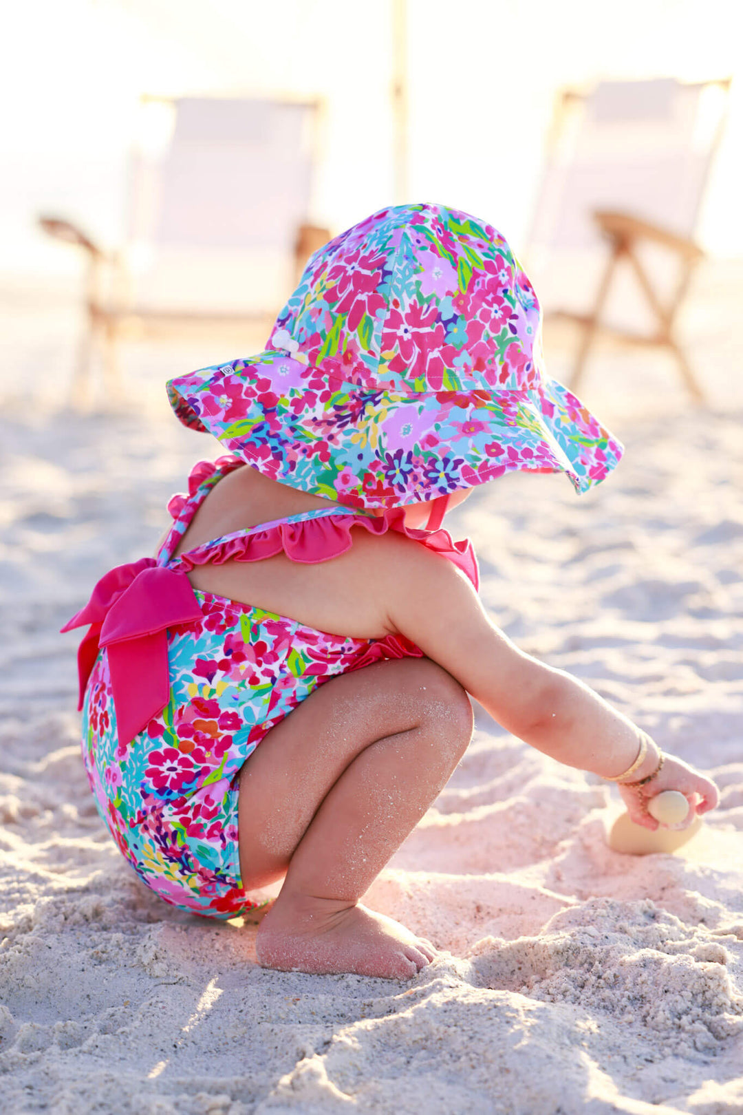 baby girl playing in the sand on the beach in petal splash double ruffle one piece with a matching sun hat 