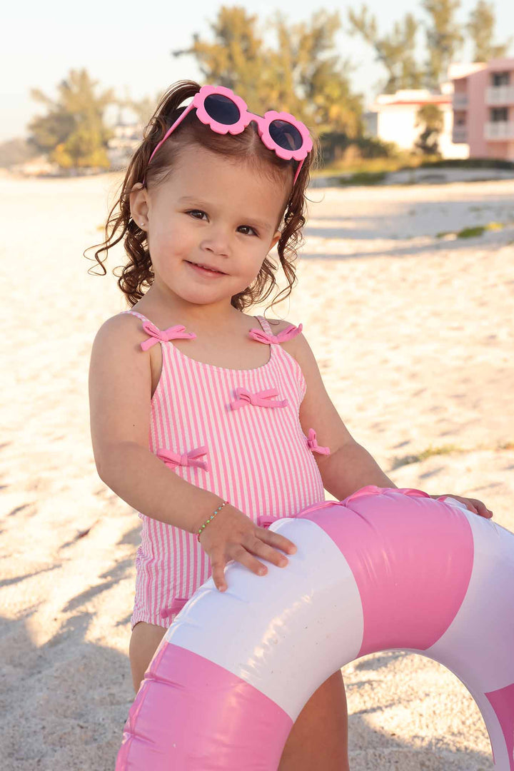 girl on beach holding innertube wearing the pink seersucker multi bow one piece swimsuit 