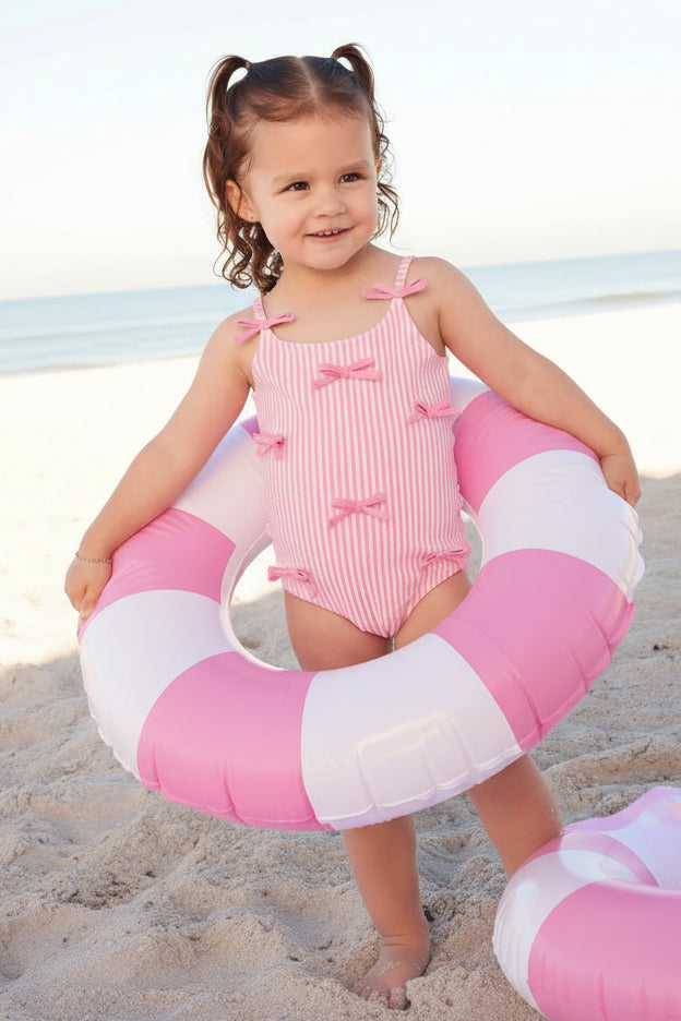 girl standing in innertube wearing pink seersucker one piece swimsuit with multiple bows 