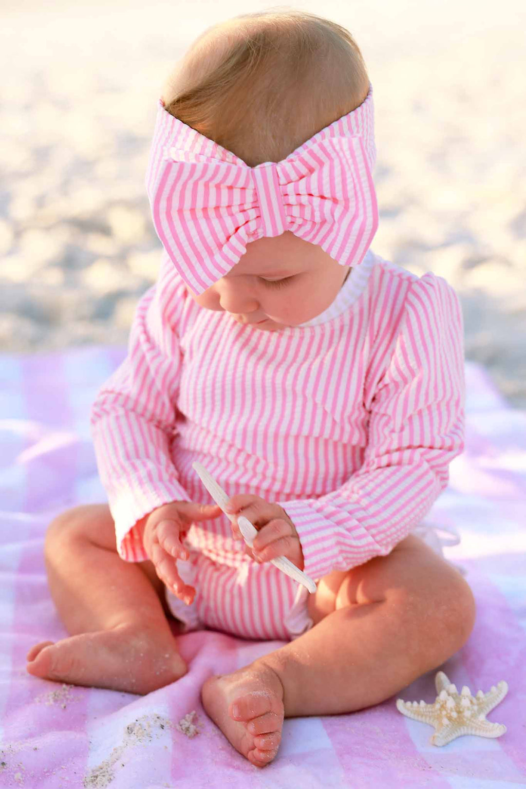 baby girl looking down wearing pink seersucker rash guard swimsuit and swim bow