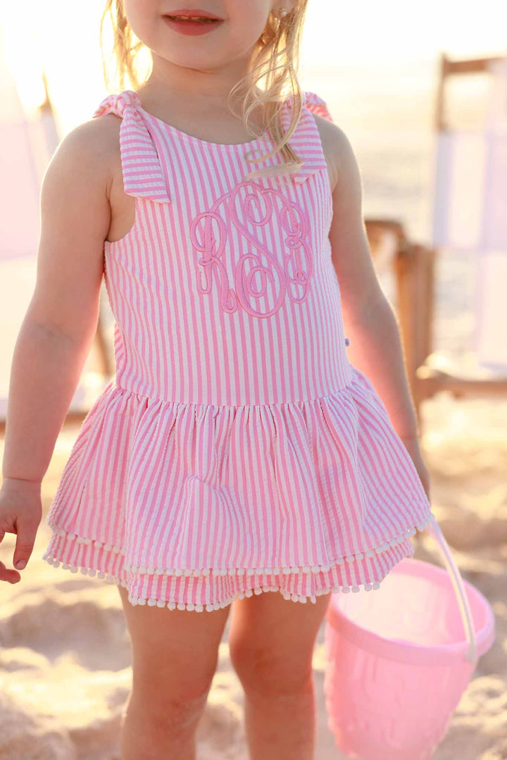 girl wearing pink seersucker tiered skirt one piece holding a pink beach bucket 