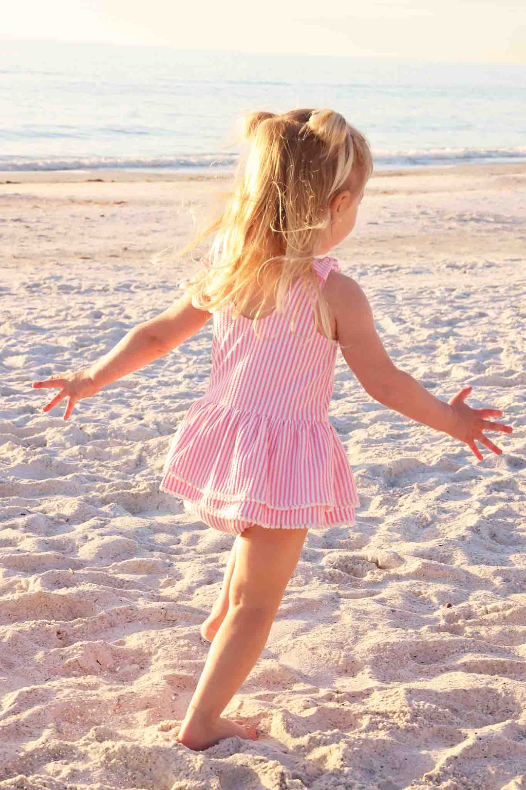 girl running on the beach in pink seersucker one piece swimsuit with tiered skirt 