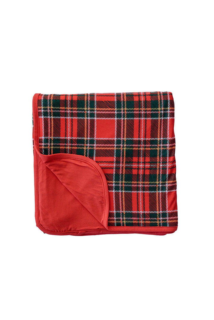 Flat lay of a folded Caden Lane double-sided bamboo blanket in a Plaid Tidings print featuring red, green, and navy tartan, with a solid red reverse.