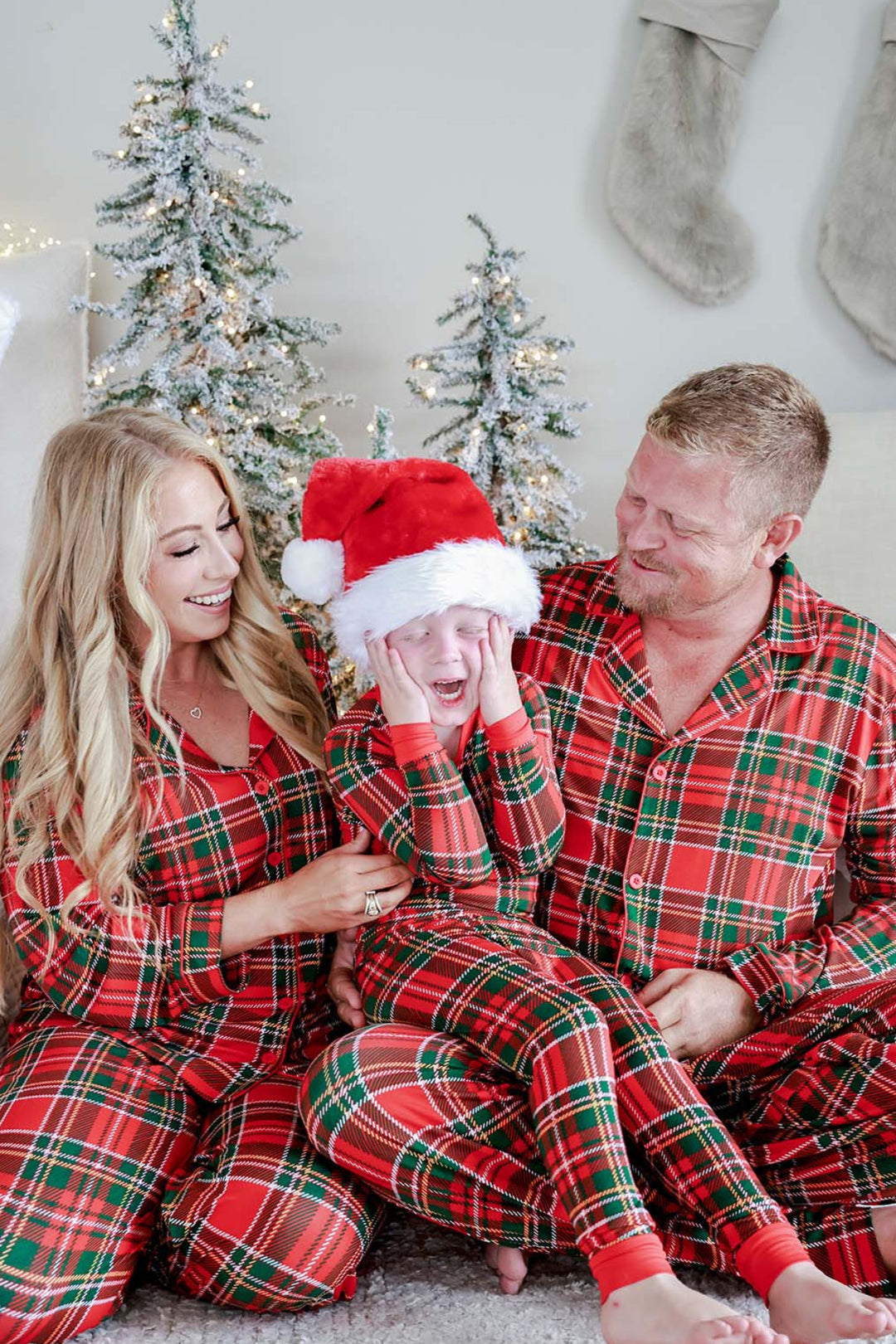 Two children laughing together in matching Caden Lane Christmas bamboo plaid pajamas, showcasing festive holiday family sleepwear in a classic red and green tartan print.