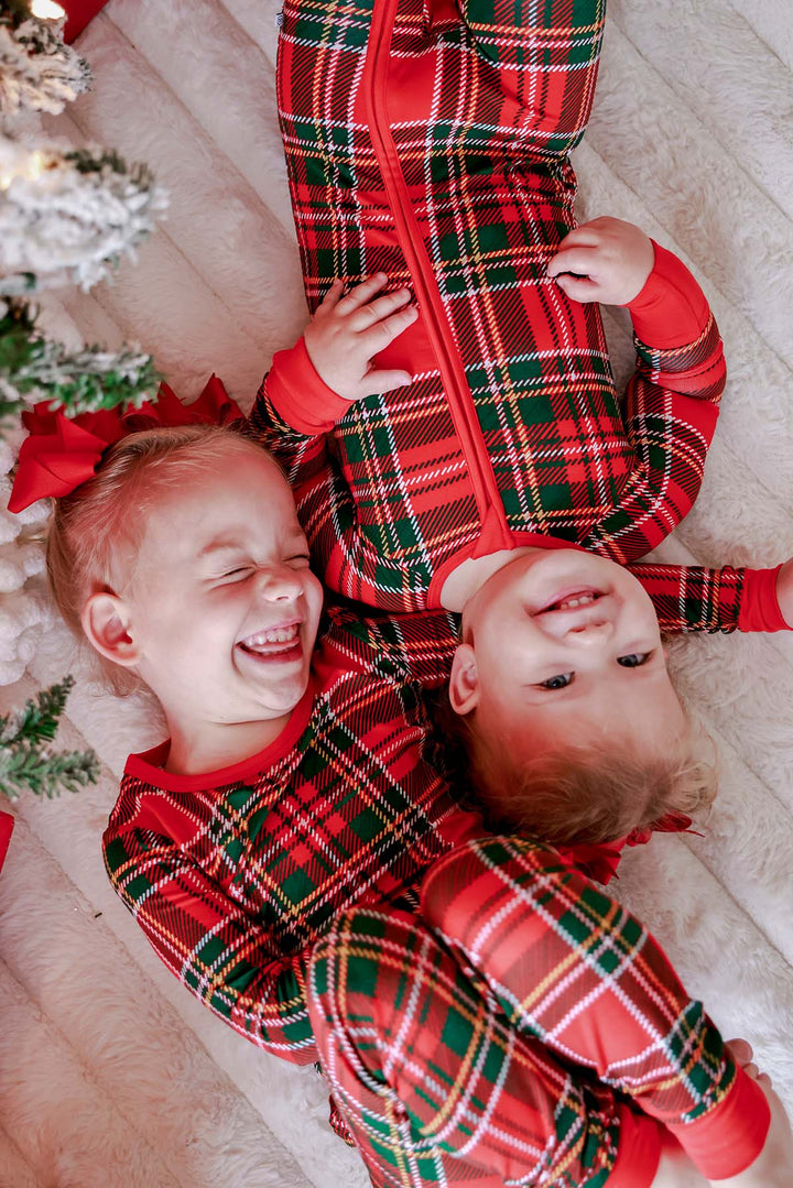 Two children laughing together in matching Caden Lane Christmas bamboo plaid pajamas, showcasing festive holiday family sleepwear in a classic red and green tartan print.