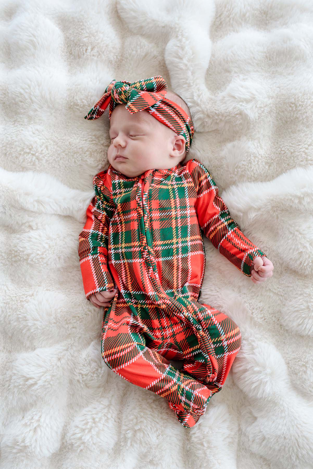 Sleeping newborn wearing a Caden Lane Christmas bamboo convertible zipper footie and matching plaid bow headwrap in a classic red tartan print, perfect for baby's first Christmas, holiday photos, and festive family matching pajamas