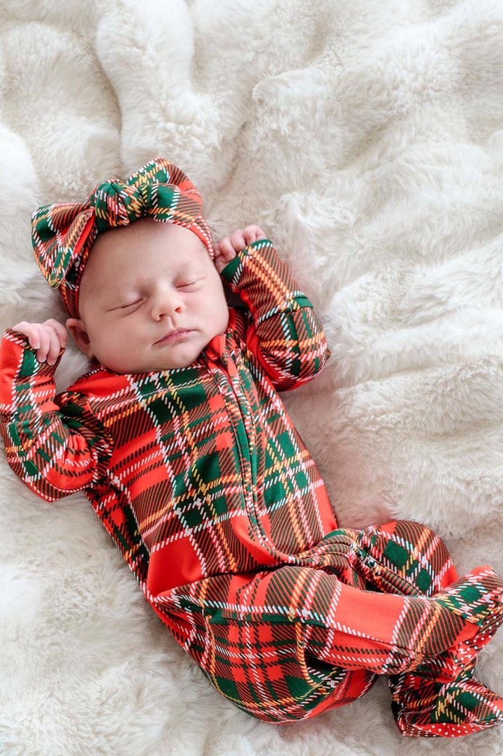 Sleeping newborn wearing a Caden Lane Christmas bamboo convertible zipper footie and matching plaid bow headwrap in a classic red tartan print, perfect for baby's first Christmas, holiday photos, and festive family matching pajamas