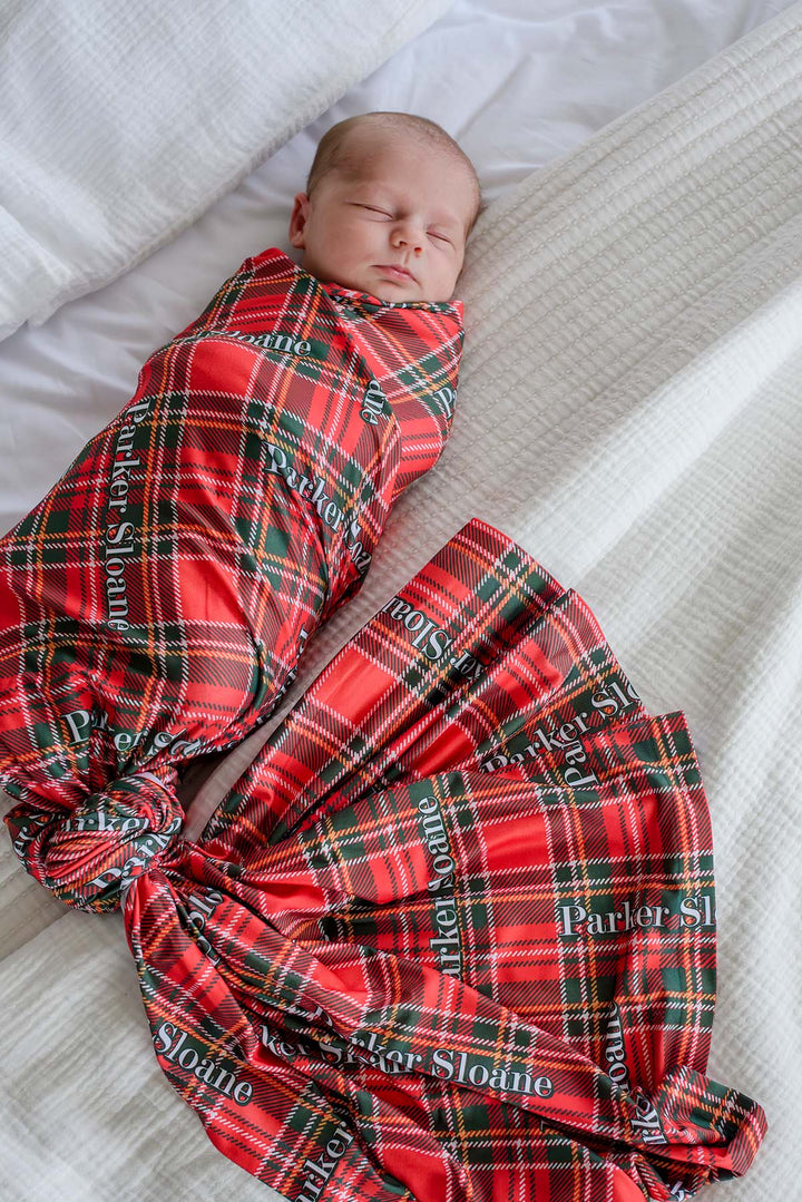 Caden Lane personalized Christmas baby swaddle blanket in a classic red and green plaid print, featuring a custom name for a cozy newborn swaddle and baby's first Christmas keepsake.