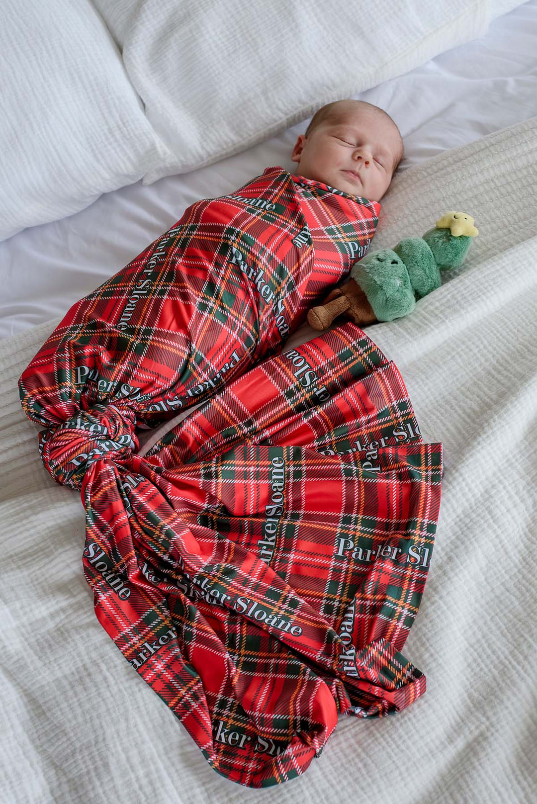 Sleeping newborn wrapped in a Caden Lane personalized Christmas swaddle blanket with a classic plaid print and custom name, perfect for hospital photos, newborn announcements, and holiday gifts.