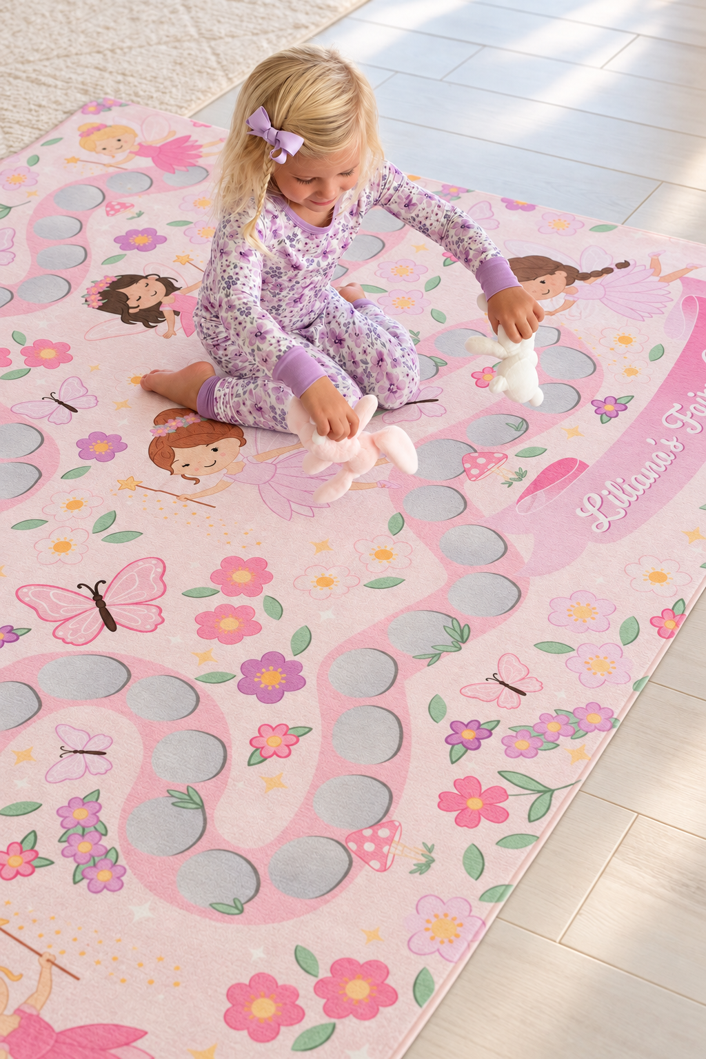 Young girl playing with plush toys on a personalized Caden Lane fairy-themed kids’ rug with flowers, butterflies and stepping-stone paths.