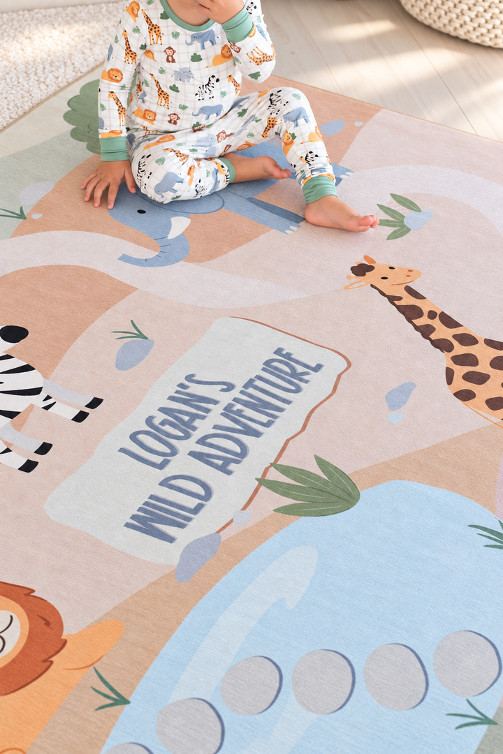 Toddler sitting on a personalized Caden Lane safari-themed kids’ rug with colorful elephants, a giraffe, zebra and lion.