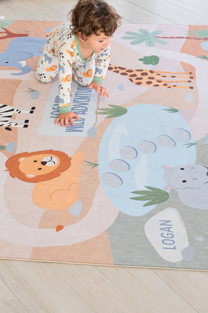 Toddler crawling across a personalized Caden Lane safari playroom rug decorated with a lion, giraffe, elephant, hippo and palm trees.