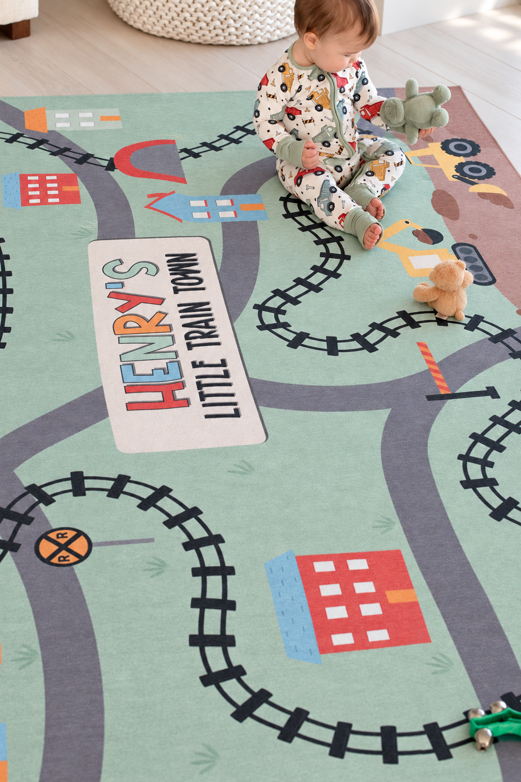Baby sitting on a personalized Caden Lane train-themed playroom rug with colorful tracks, roads, buildings and construction vehicles.