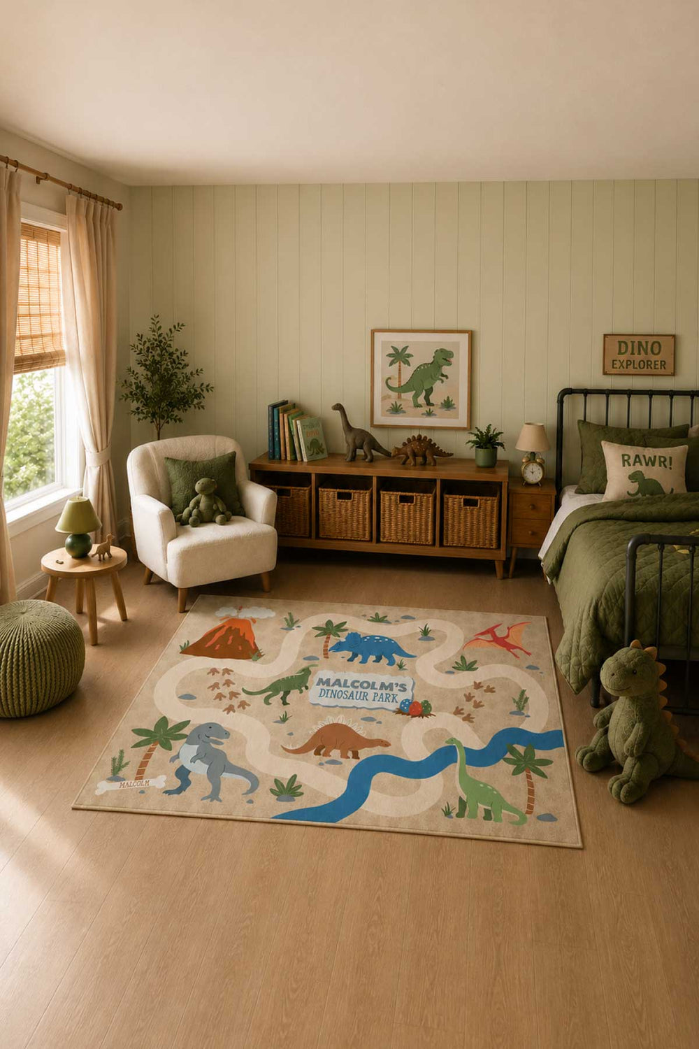 Caden Lane personalized dinosaur-themed area rug in a boy's bedroom, featuring a tan play-map design with a volcano, river, palm trees, and colorful dinosaurs surrounding the text 'Malcolm's Dinosaur Park,' placed on a wood floor near a bed with dinosaur-print pillow and stuffed dinosaur toys
