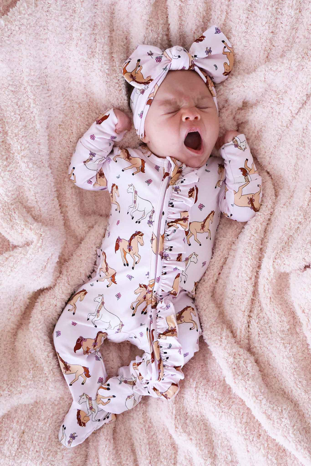 yawning baby girl in pony club pink ruffle zipper footie with matching headwrap 