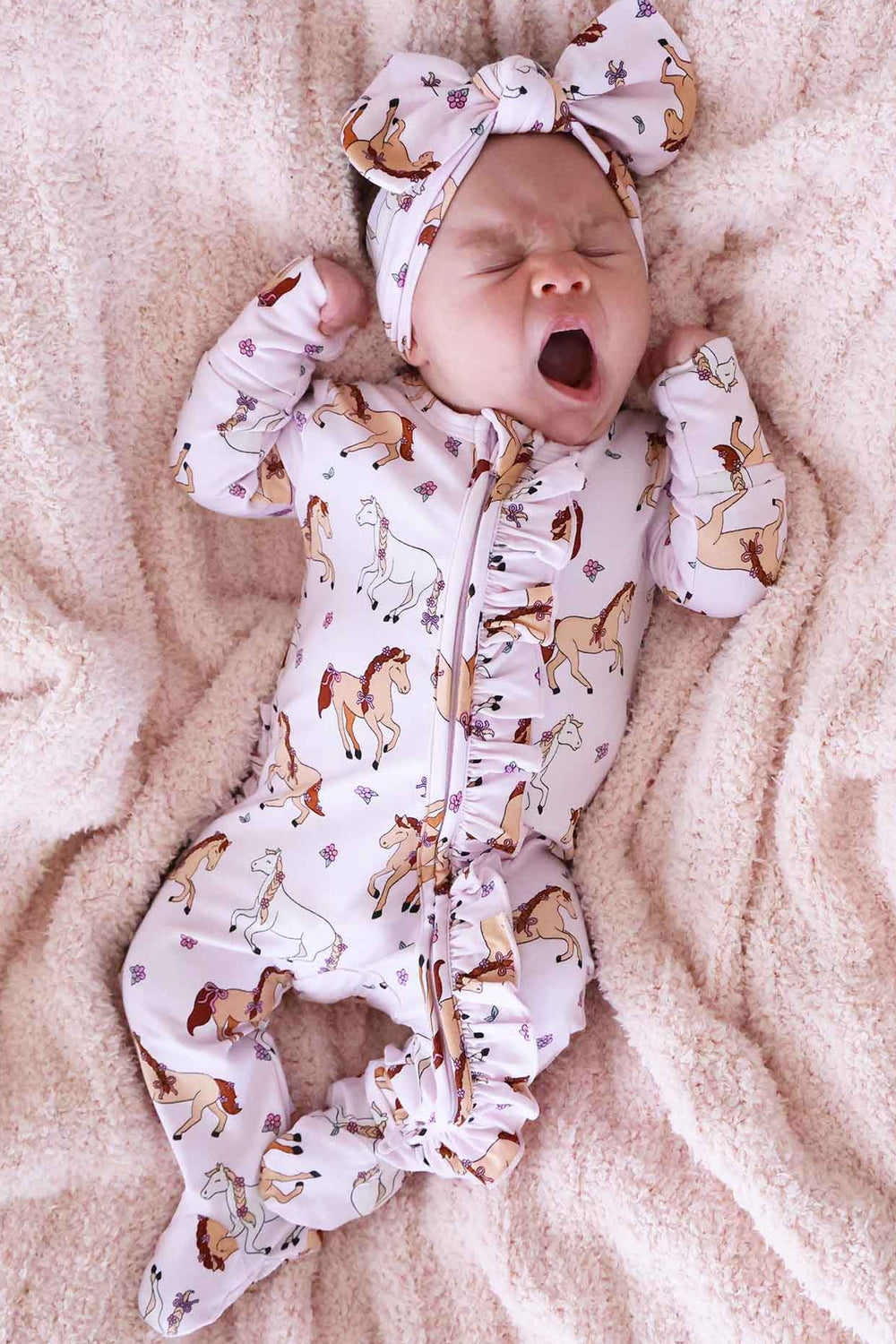 Baby in a Pony Club onesie with a matching headband on a soft surface