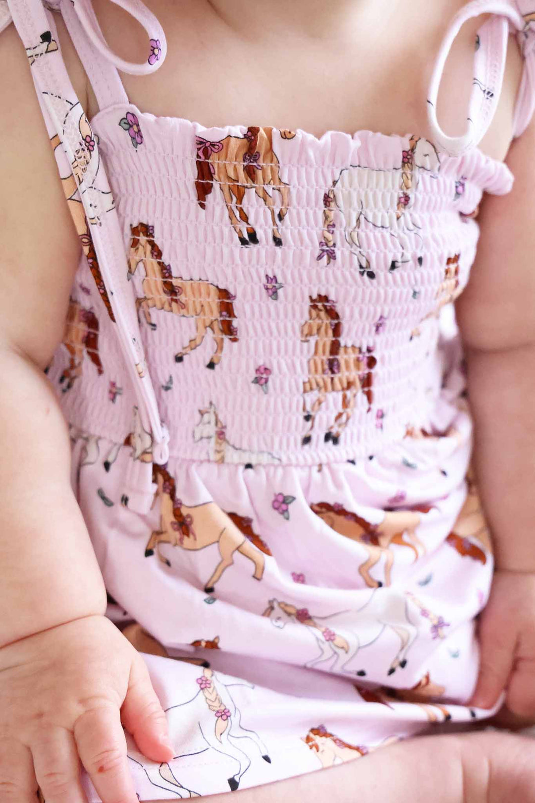 closeup of smocked top romper for girls in pony club pink print 