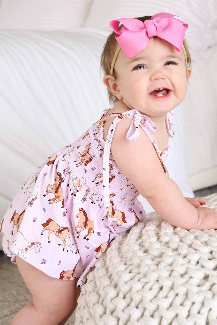 baby girl leaning on ottoman wearing pony club pink smocked romper 