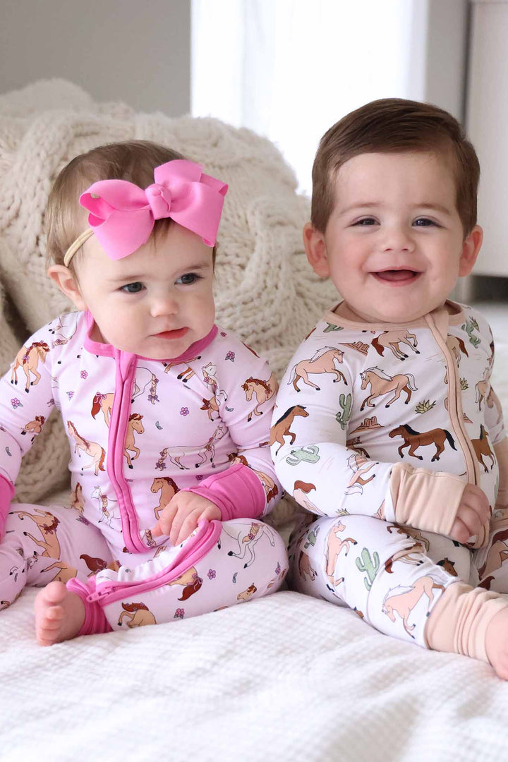 Baby girl on the left is wearing the Pink Pony Club zip romper and baby boy on the left is wearing the neutral Pony Club zip romper. 