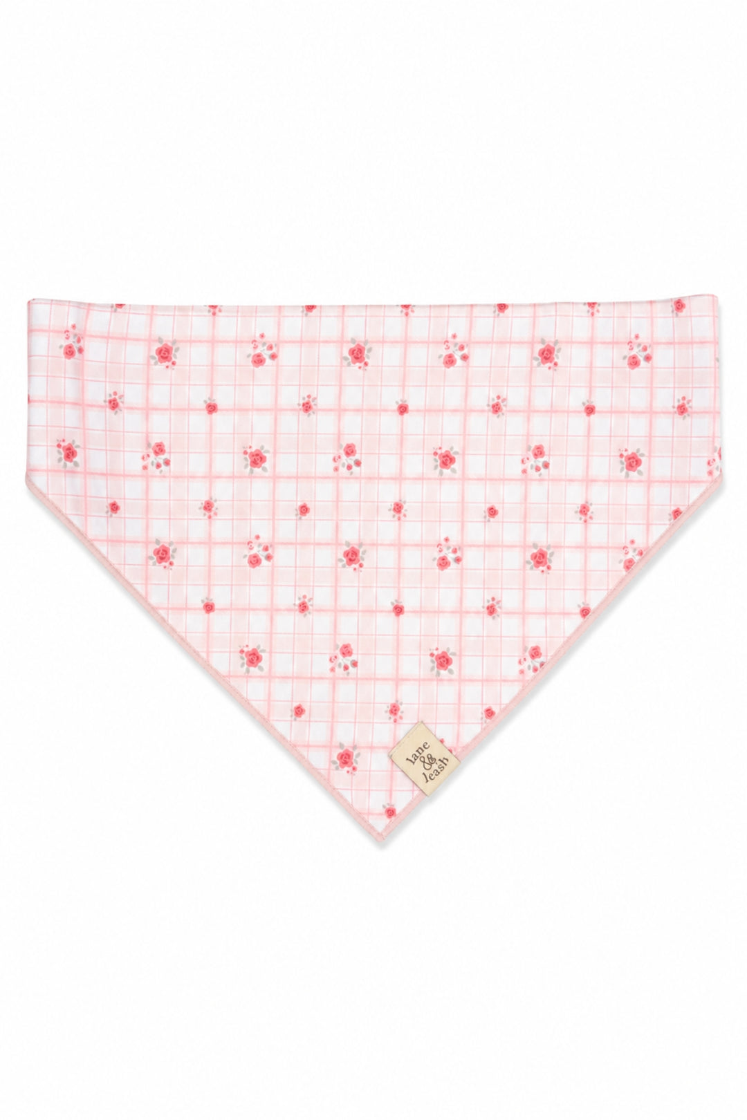 A triangular Lane & Leash bandana-style pet bib in white fabric with a light pink grid pattern and small pink floral motifs, featuring a small beige fabric brand tag near the bottom point.