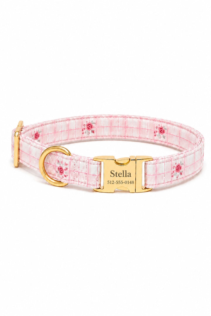 A Lane & Leash pink and white plaid dog collar with a small red rose pattern, featuring a gold-tone metal buckle engraved with the name 'Stella' and a gold D-ring.