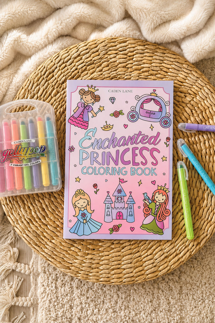 Caden Lane Enchanted Princess Coloring Book styled on a woven rattan tray with a cream throw blanket, next to a Gellypop gel crayon case and pastel Caden Lane markers