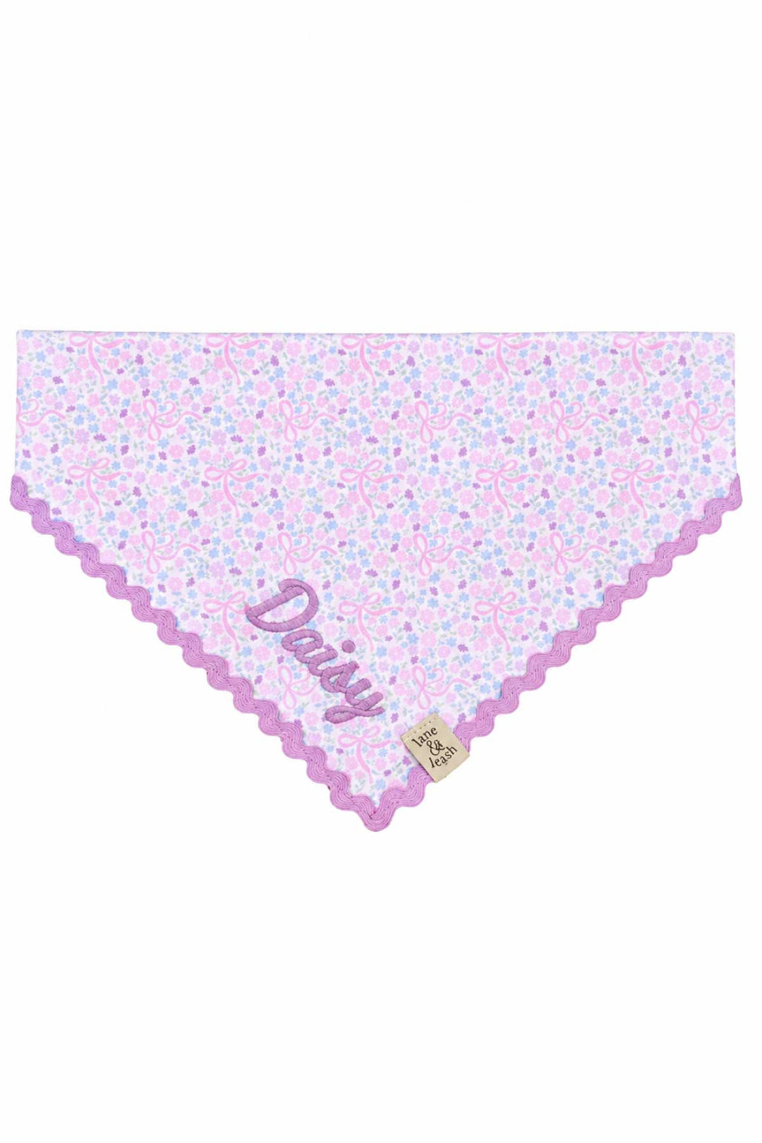 Embroidered pet bandana in the Ribbon Garden print — soft pink and lavender floral fabric with a purple scalloped embroidered edge — displayed flat in a triangle shape, personalized with the name "Daisy"