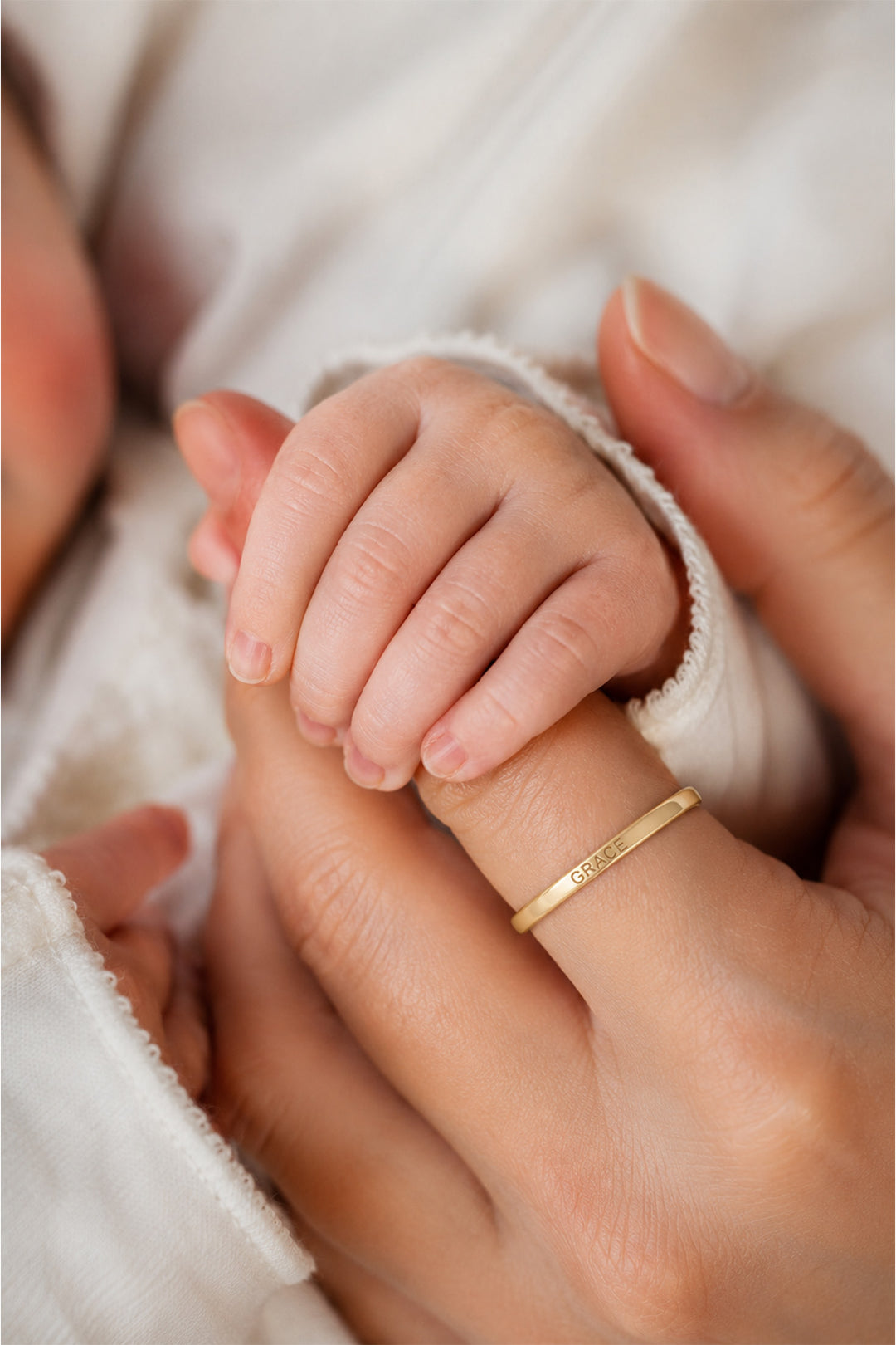 Caden Lane personalized gold name ring engraved with Grace worn by a mother holding her newborn baby's hand.