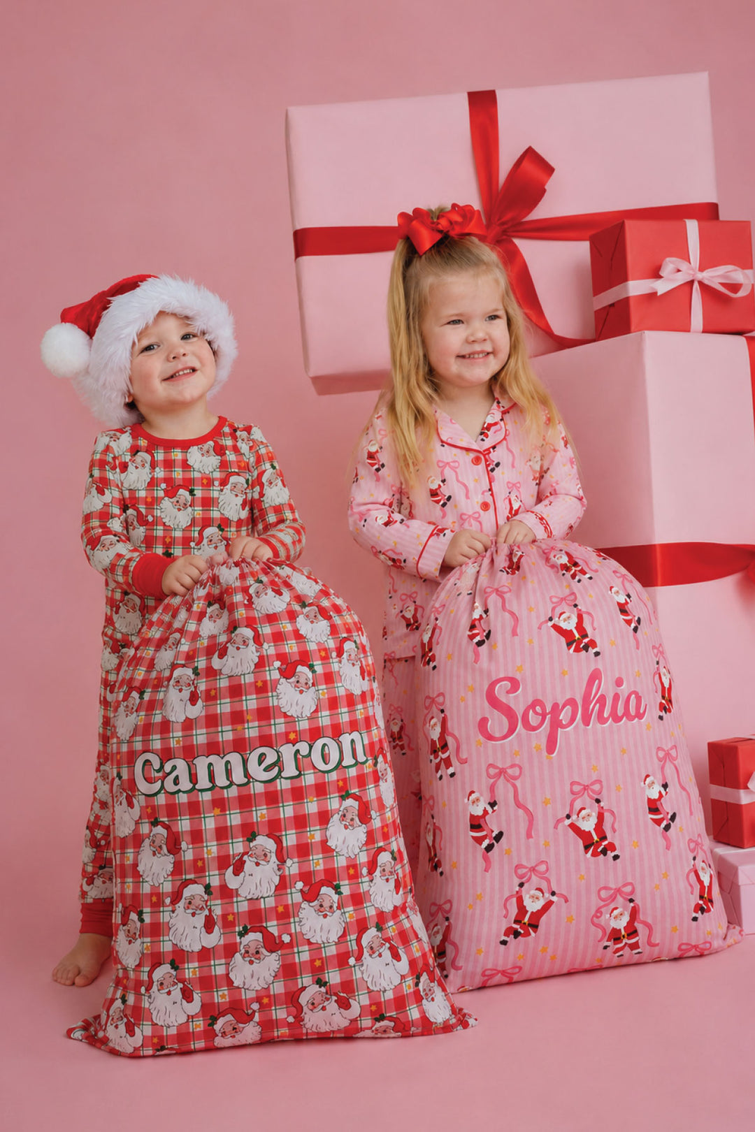 Two children wearing matching Caden Lane Christmas pajamas hold personalized Santa sacks in Cozy Claus and Pink Merry collections, perfect for personalized Christmas gifts, holiday traditions, and Christmas morning surprises.