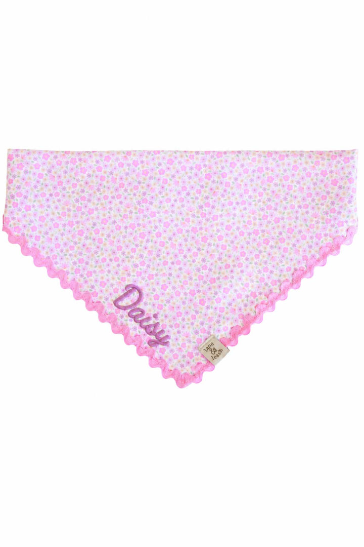 Flat lay of embroidered pet bandana in Scattered Blooms print with pink ric-rac edge trim and pet name embroidered in script at the front tip