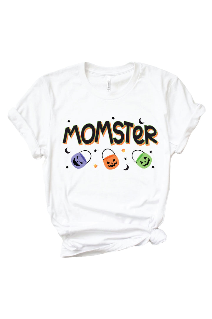 White adult t-shirt with black 'MOMSTER' lettering outlined in orange, small crescent moons, and three colorful jack-o-lantern candy bucket icons below