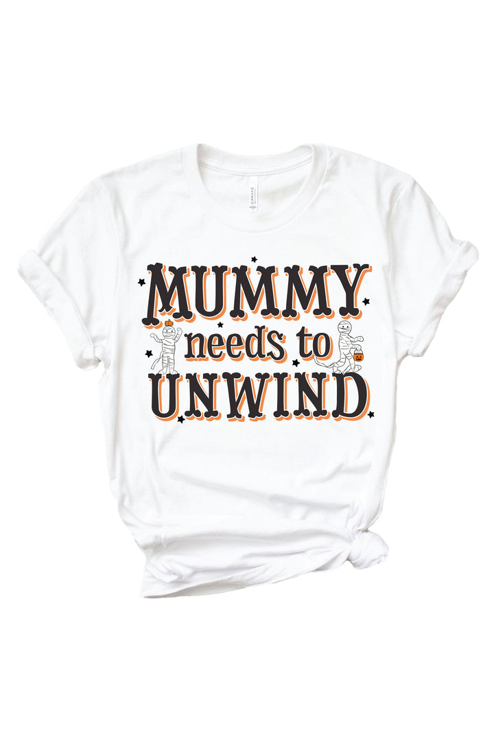 White Caden Lane Halloween t-shirt for women featuring 'Mummy Needs to Unwind' text in black and orange lettering with two cartoon mummy characters holding pumpkin treat buckets, surrounded by black star accents