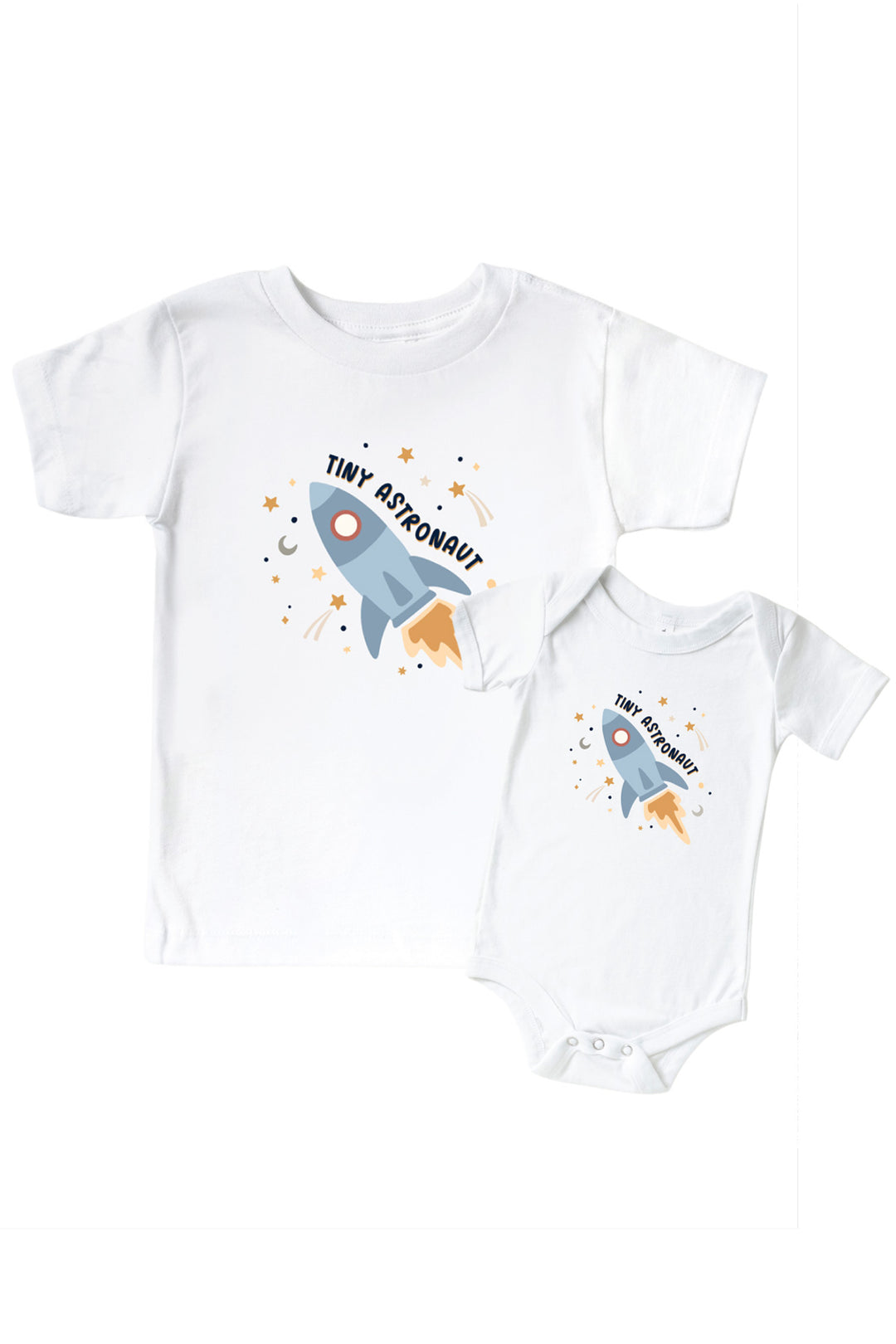 Flat lay of a matching Caden Lane white kids’ tee and bodysuit pair with a Stellar Snuggles graphic featuring a blue rocket, reading “Tiny Astronaut.”