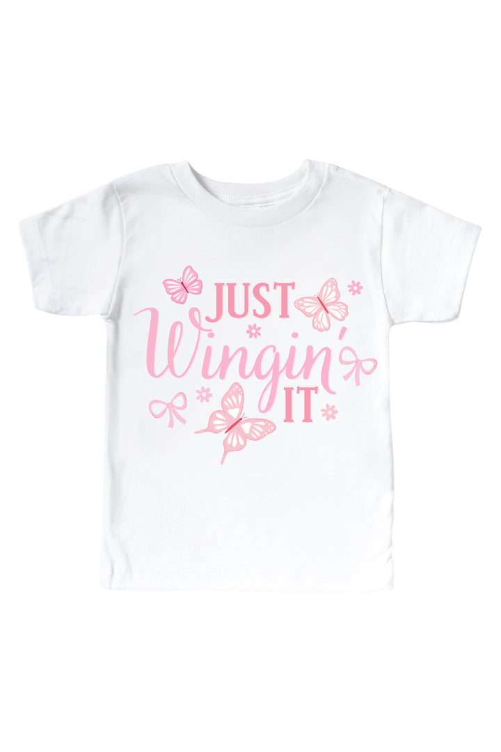 Just Wingin' It Graphic Kids Tee in Blooming Butterflies print - white tee featuring pink "Just Wingin' It" text with butterfly and bow accents