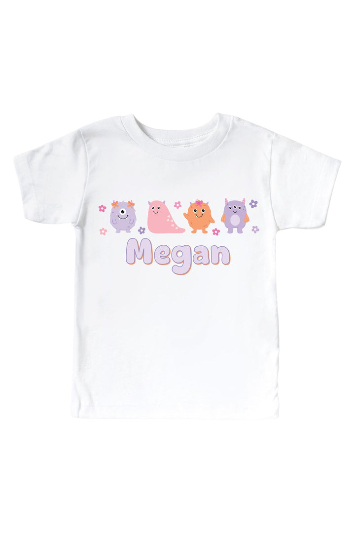 Caden Lane white kids t-shirt personalized with "Megan" in purple lettering, featuring pink, purple, and orange cartoon monsters and flowers