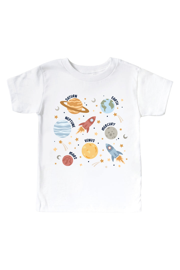 Flat lay of a Caden Lane white kids’ tee with a Stellar Snuggles graphic featuring a rocket, Saturn, Mars, and Earth among stars, reading “Nathan.”