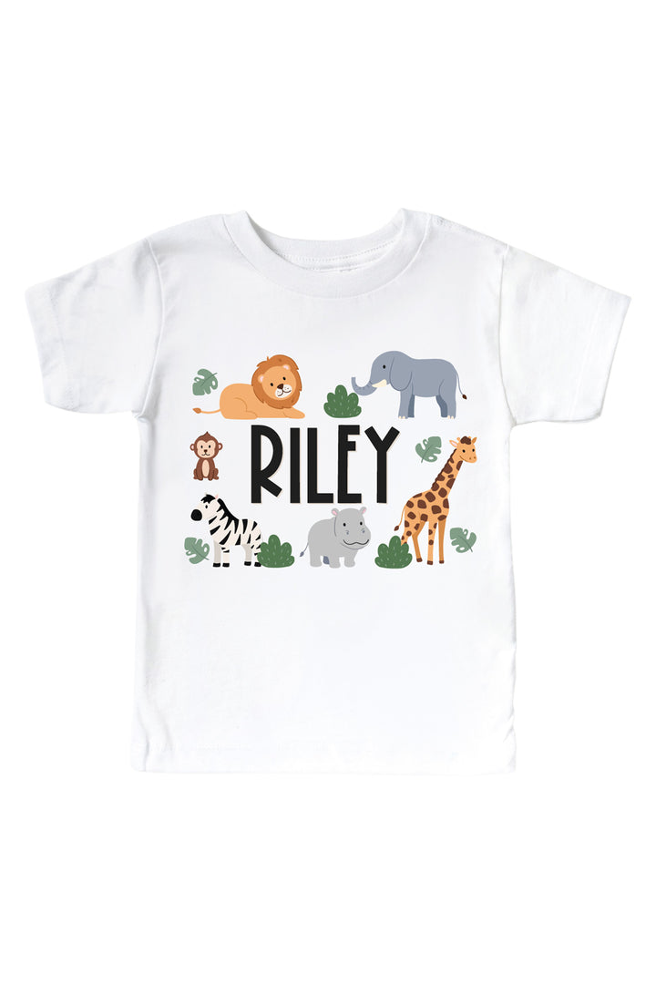 Caden Lane personalized white kids' t-shirt with the name "Riley" surrounded by safari animal illustrations — lion, elephant, monkey, zebra, hippo, and giraffe.
