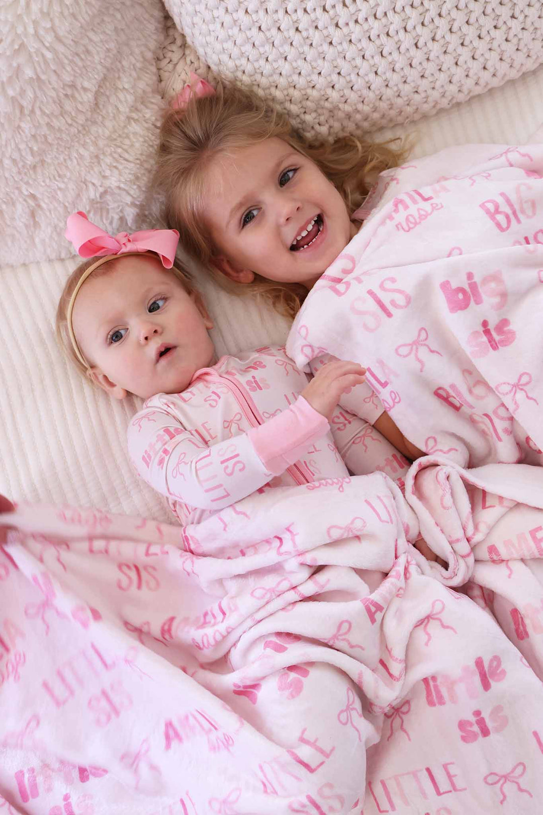 sisters laying next to each other with personalized blanket over them 