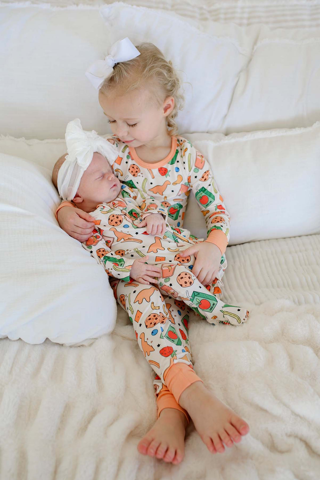 Close-up of newborn's feet and legs wearing the Snack Attack Ruffle Bamboo Zipper Footie, with the ruffle detail and snack print showing juice cartons, dinosaur crackers, and various snack motifs on cream fabric