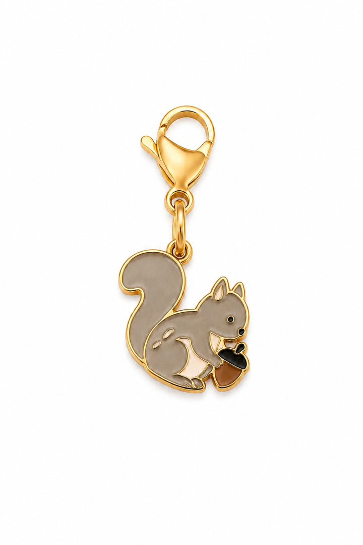 A Lane & Leash gold-plated squirrel charm with a  clasp, featuring a gray and white enamel squirrel holding a small brown acorn on a plain white background.