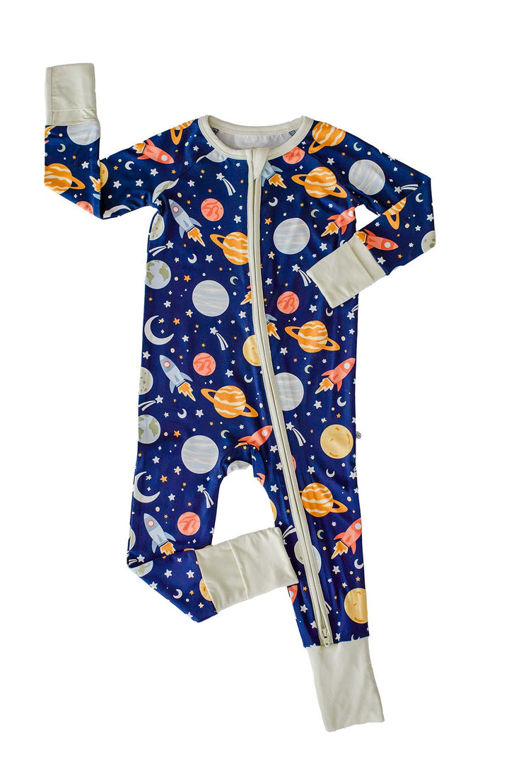 Flat lay of a Caden Lane navy bamboo zip romper arranged in a playful pose with fold-over cuffs, in a Stellar Snuggles print featuring planets, rockets, and stars.