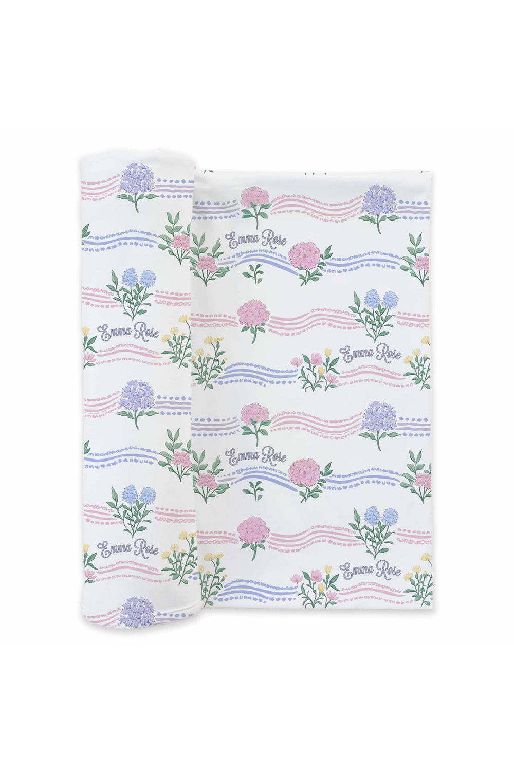 Flat lay of a partially unrolled Caden Lane white knit swaddle in a Hydrangea Garden print featuring blue hydrangeas, pink peonies, and wavy pastel ribbons, reading "Emma Rose."