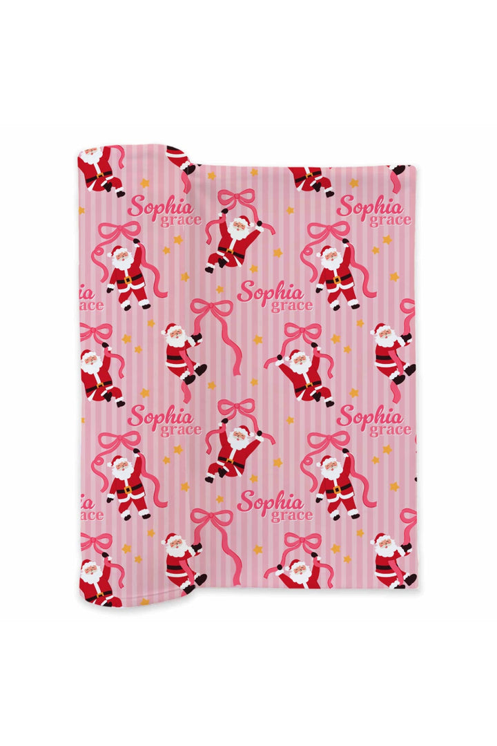 Caden Lane Personalized Jolly Ribbons Bamboo Swaddle Blanket featuring custom name personalization with festive Santa, ribbon bow, pink stripe, and holiday star print.