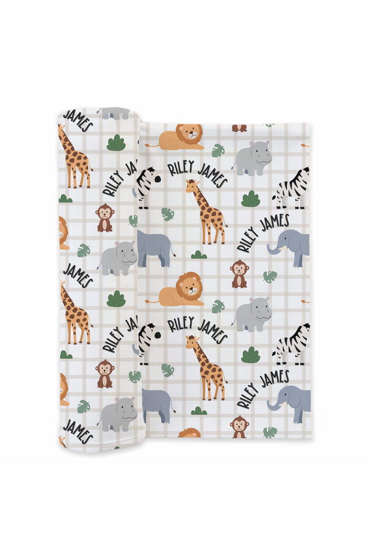 Partially rolled Caden Lane personalized swaddle blanket in a Wild Child print featuring lions, giraffes, elephants, zebras, hippos and monkeys on cream plaid, with arched name text reading "Riley James."